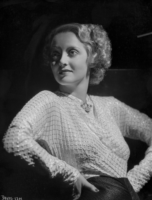 Bette Davis Posed Hands on the Waist and Looking to the Right in Glossy Long Sleeve High Neck Dress and Black Skirt Photo Print - Item # VARCEL693025