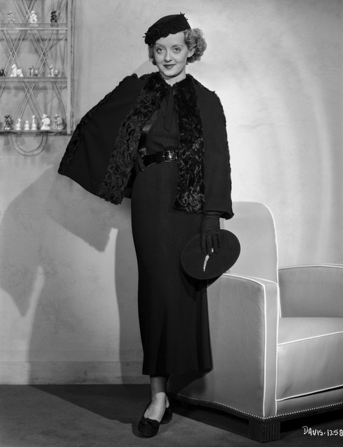Bette Davis Posed Beside a Couch in Black Long Sleeve Lace Long Dress and Black Flat Cap Photo Print - Item # VARCEL693037