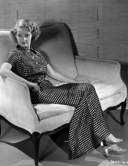 Bette Davis Seated on a White Couch with Arms on the Chair Arm and Hand on the Lap in Black Polka Dot Dress Photo Print - Item # VARCEL693118