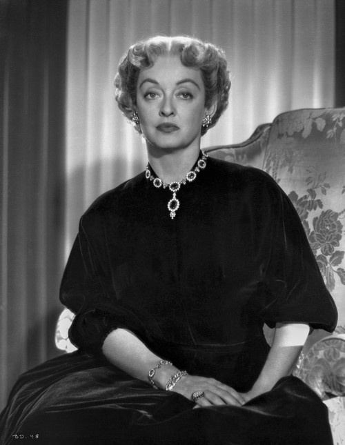 Bette Davis Seated on a Couch with Hands Together Laid on the Lap in Black Silk Dress and Gem Necklace with Marcel Wave Hair Photo Print - Item # VARCEL693155