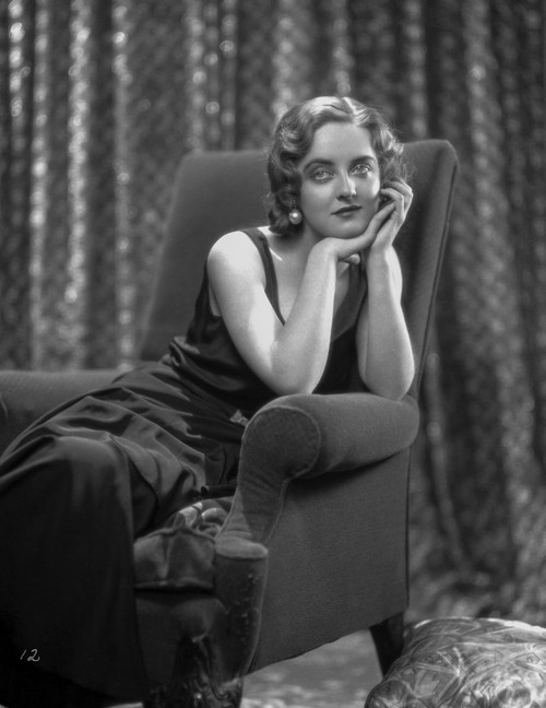 Bette Davis Seated on a Black Couch with Chin Leaning on Hand in Black Velvet Dress with Marcel Wave Hair Photo Print - Item # VARCEL693247