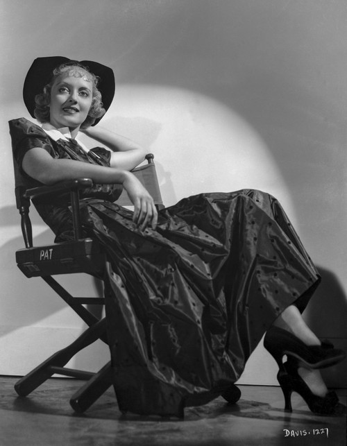 Bette Davis Seated on a Director's Chair in Black Hat and Black Dress with White Collar Photo Print - Item # VARCEL693385