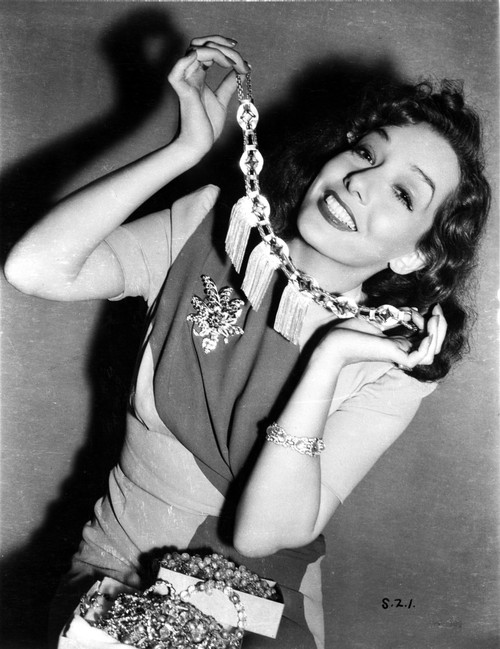 Lupe Velez smiling in Elegant Dress while Putting on Her Necklace Photo Print - Item # VARCEL705349