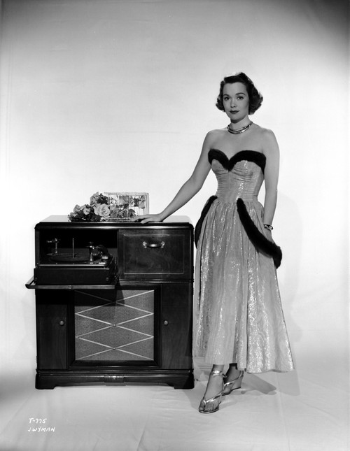 Jane Wyman Posed in White Silk Dress with Gathered Long Skirt with Right Hand on the Radio Box Photo Print - Item # VARCEL705882