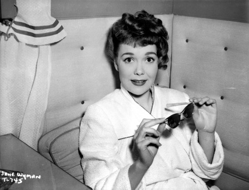 Jane Wyman Seated on the Leather Couch in White V-Neck Long Sleeve Tweed Linen Shirt with Hands Holding a Sunglasses Photo Print - Item # VARCEL705912
