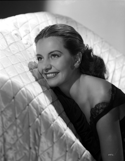 Cyd Charisse smiling in a White Couch wearing Black Sleeveless Dress and an Earrings Photo Print - Item # VARCEL706445