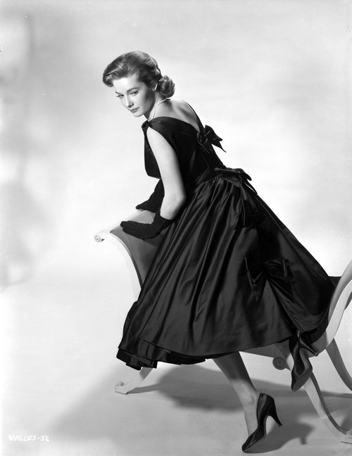 Vera Miles kneeling onto a chaise lounger, looking behind her shoulder, wearing a black, sleeveless gown with bows elegantly placed along the back Photo Print - Item # VARCEL706571