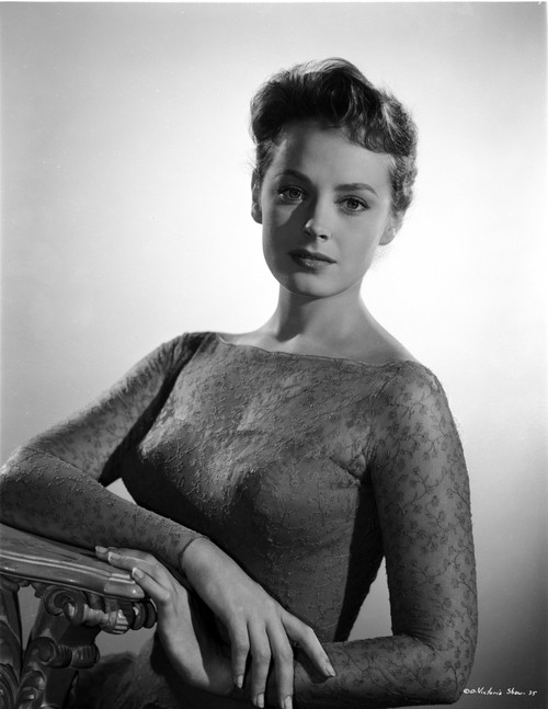 Victoria Shaw leaning one arm on a tabletop, while wearing a wearing a sweetheart neck line, ballgown, with a long-sleeve lace over-lay Photo Print - Item # VARCEL707987