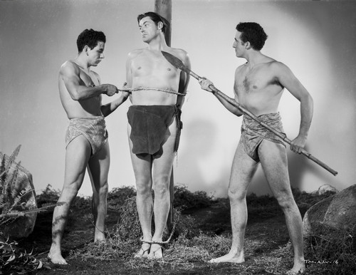 Johnny Weissmuller Tied Up in a Pole and Being Threatened by Two Guys in a Movie Scene Photo Print - Item # VARCEL709329