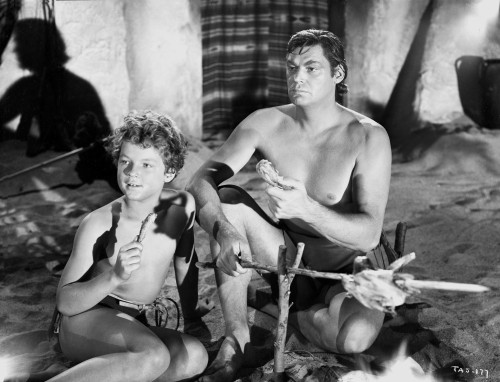 Johnny Weissmuller Looking Away with a Boy while Grilling Chicken in a Movie Scene Photo Print - Item # VARCEL709373
