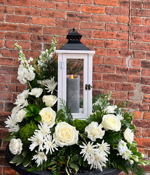 A serene arrangement featuring soft white roses, elegantly surrounding a lantern, symbolizing hope and eternal light during times of sorrow