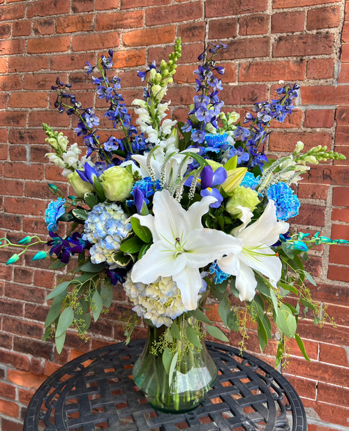 A captivating arrangement where pristine white lilies meet the deep allure of blue orchids. Tall, striking blue blooms reach skyward while lush greenery drapes downward, creating a beautiful blend of vibrancy.
