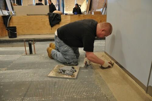 Worker applying a concrete cove mortar along the floor-wall joints.