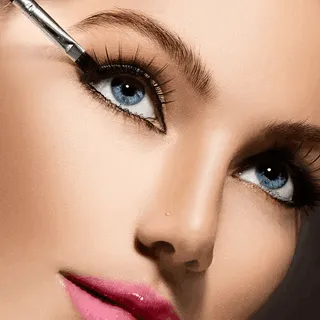 A woman with striking blue eyes carefully applies mascara to enhance her lashes and create a captivating look.