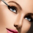 A woman with striking blue eyes carefully applies mascara to enhance her lashes and create a captivating look.