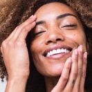 A woman with curly hair smiling warmly, radiating joy and happiness.