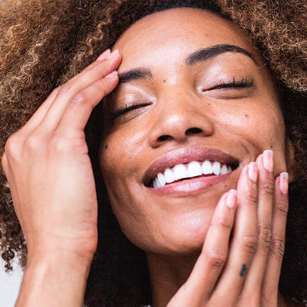 A woman with curly hair smiling warmly, radiating joy and happiness.