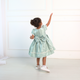 Discover the enchantment of our mint green dress for girls - a dreamy creation adorned with glossy satin, puffy sleeves, and delicate pearl trim. Featuring a charming bow in front and back, this dress is beautifully lined with soft cotton fabric for ultimate comfort