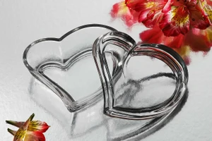 A clear crystal heart on a table surrounded by colorful flowers, perfect for wedding or bridal shower favors