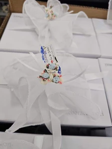 A sophisticated box wrapped in white paper, accented with a white linen pull bow and porcelain flowers, perfect for enhancing party decor.