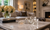 Crystal flower ornament with a jeweled curved stem displayed on a marble coffee table in an elegant, warmly lit living room with a sofa, fireplace, flowers, and decorative books in the background.