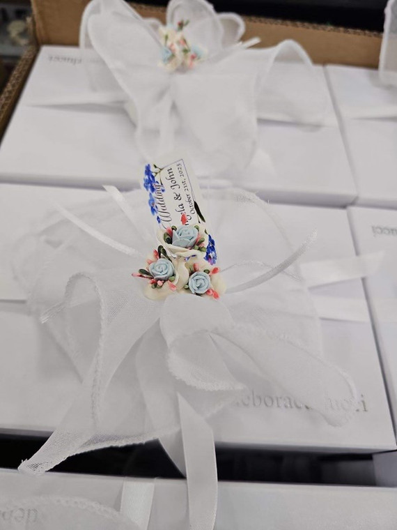 A sophisticated box wrapped in white paper, accented with a white linen pull bow and porcelain flowers, perfect for enhancing party decor.