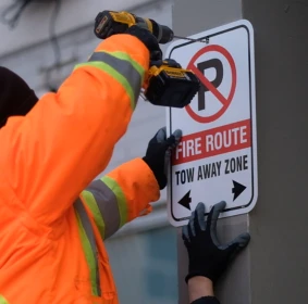 Installer in a high-visibility jacket mounting a fire route sign