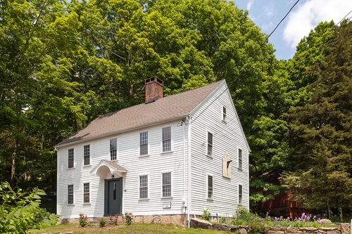 A picture of a classic New England Style House set in front of a forrest of beautiful green trees in Canada for Bardia