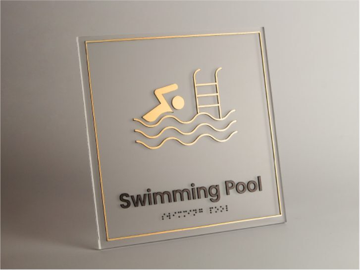 Singularum swimming pool sign with a gold pictogram, gold border and Braille
