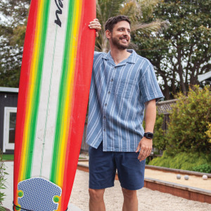 Man walking with surfboard wearing Ayden Organic Cotton Camp Shirt in blue plaid
