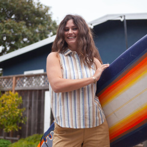 Woman standing outside with a surfboard wearing Aviva Full Button Striped Tank Top Ceramic