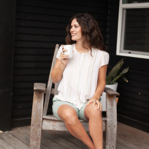 Woman sitting on chair outside wearing Pippin Pintuck Top in peach color