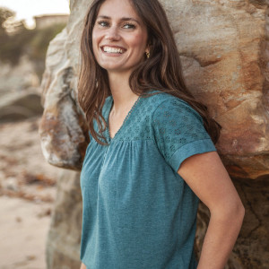 Woman leaning against rock outside wearing Ansley Eyelet Top in mallard blue color