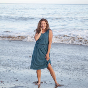 Woman standing in water on beach wearing Blue Skies Printed V-Neck Dress in Mallard Blue