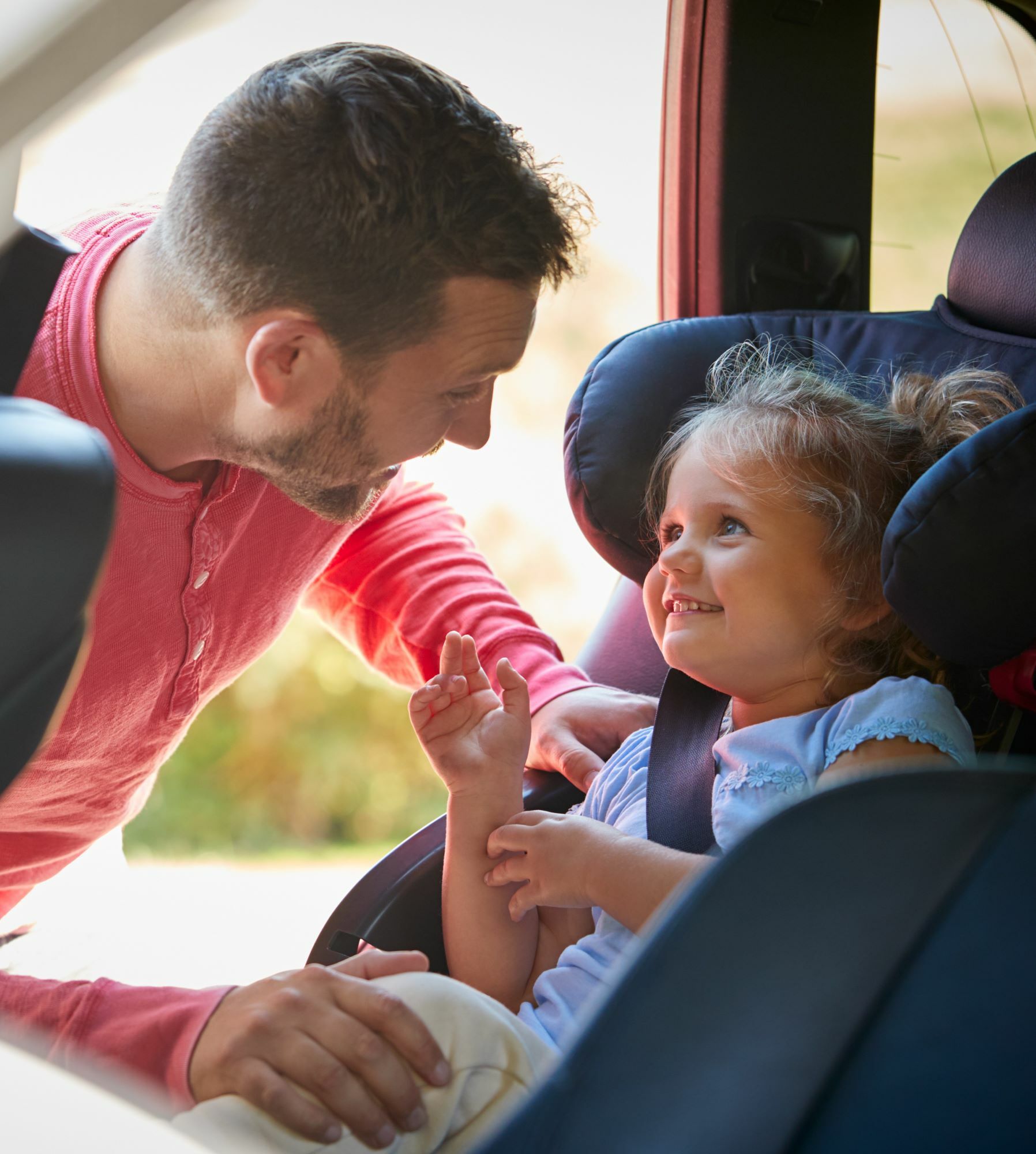 father strapping child into carseat