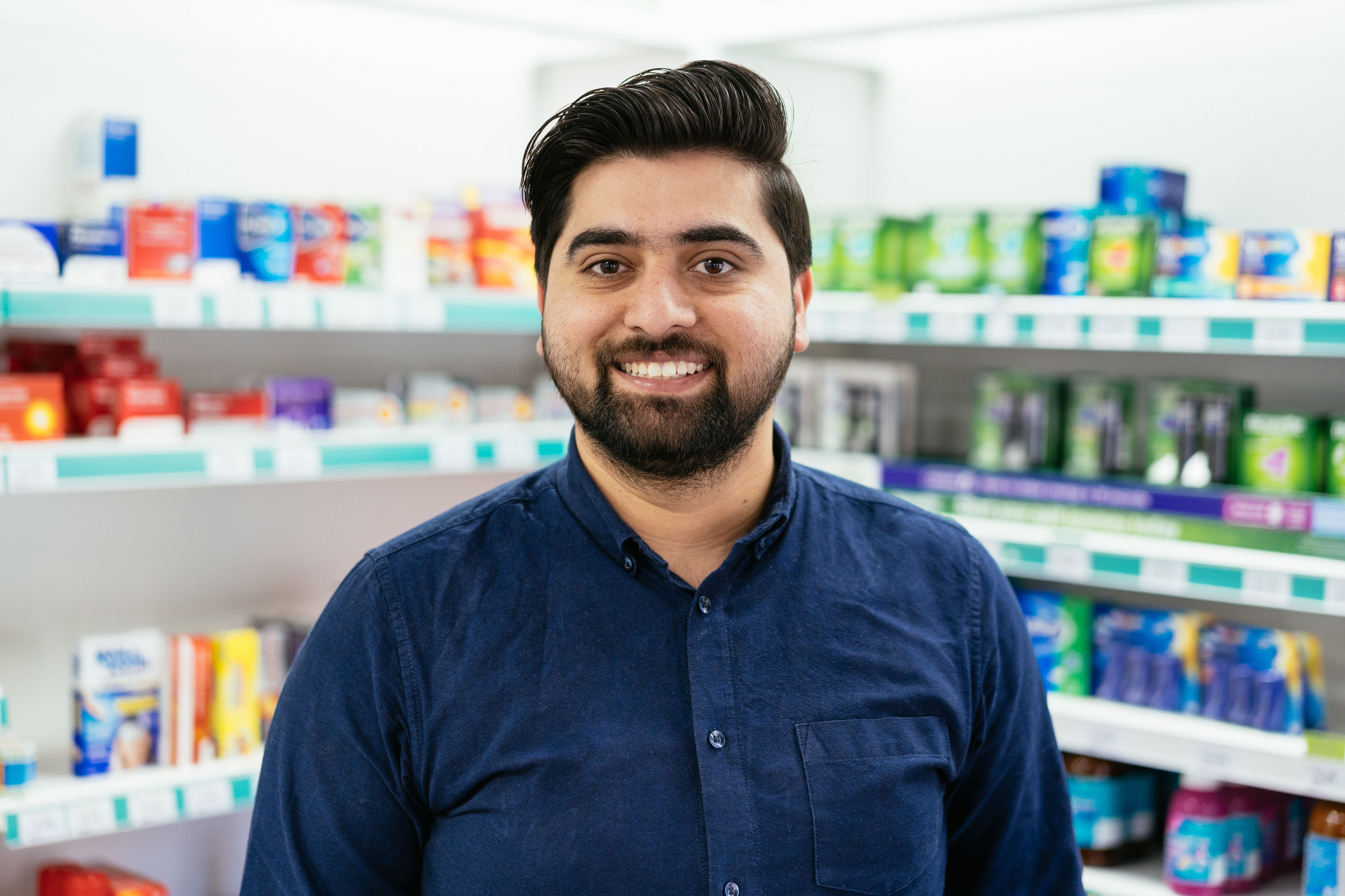 A Well pharmacist smiling in front of a medicine counter.