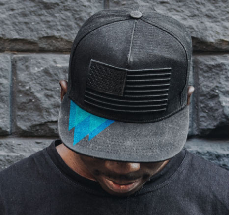 Man wearing black arctic leaf logo hat with brick wall background.