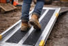 Construction worker boots walking on wet aluminum ramp with black anti-slip grip tape
