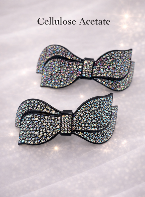 Luxe Bow Crystal Barrette: two crystal bow barrettes with iridescent stones on a sparkling pink background