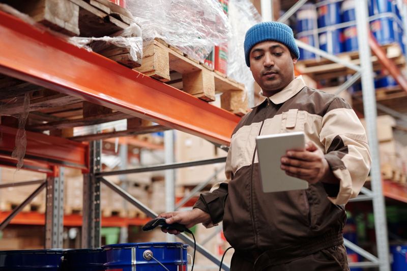 Warehouse associate checking stock on a tablet beside pallet racking