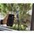 Sper Scientific Bluetooth Light Meter, hand holding a smartphone with a light measurement graph displayed, digital light meter on a tripod outdoors among green plants and rocks.
