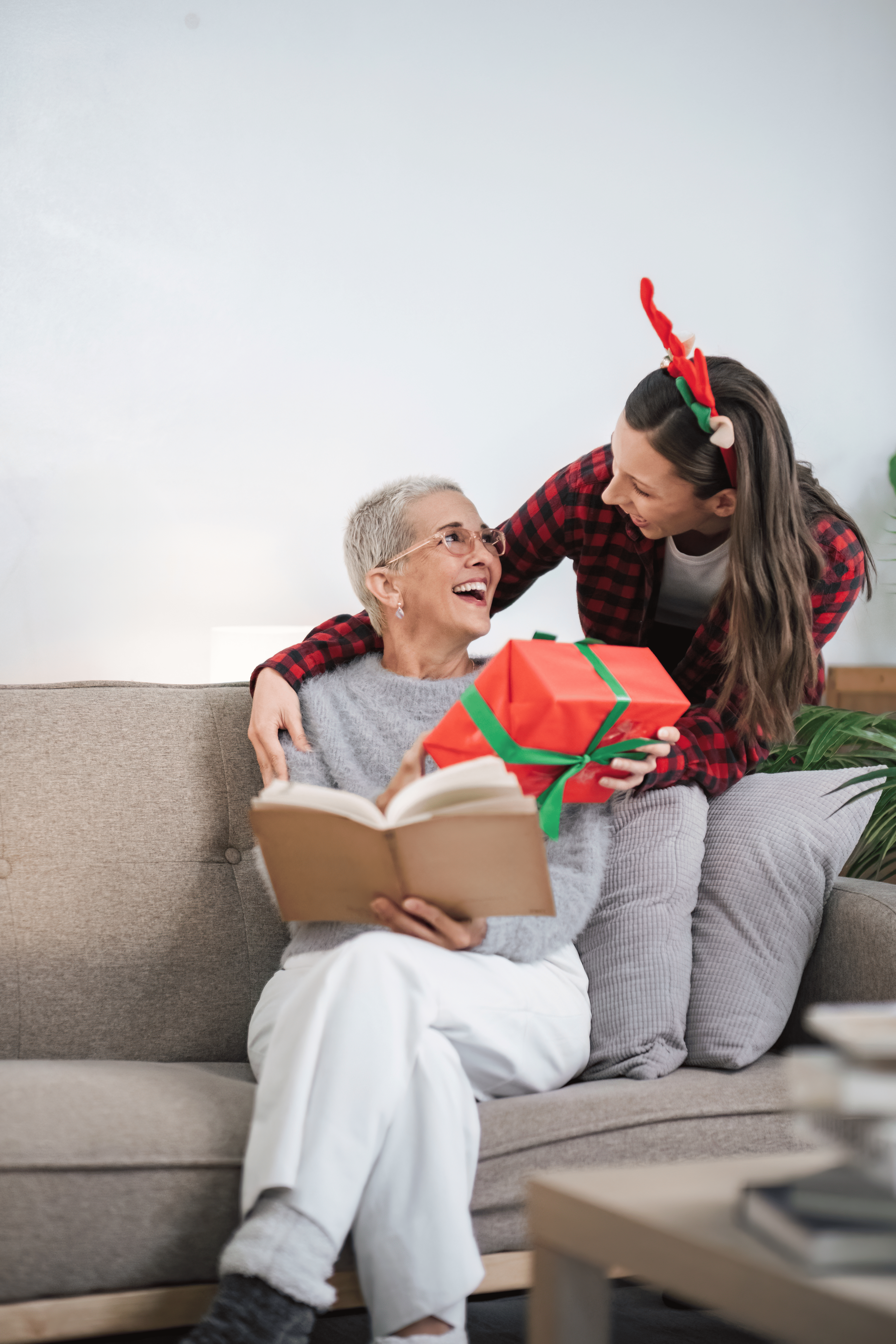 Woman gifting mother with a wrapped gift on couch.