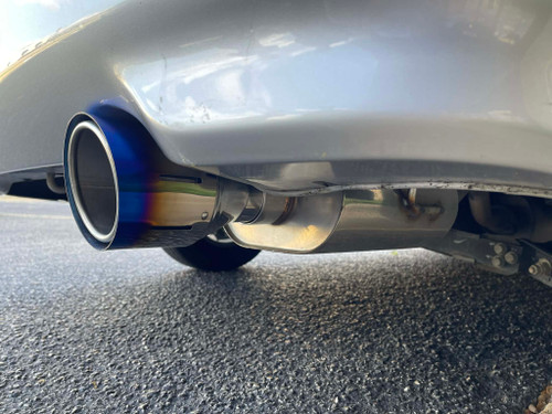Burnt titanium dual-layer exhaust tip installed on vehicle, showing slip-on fitment over factory muffler outlet.