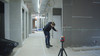 Leica Lino L6G on a tripod projecting a green line along a long corridor while a contractor measures from it