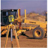 Spectra GL700 series rotary laser set up on a tripod on a construction site, with a motor grader working to grade behind it