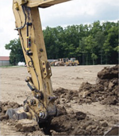 Excavator dipper arm and bucket digging a trench in dirt on a jobsite