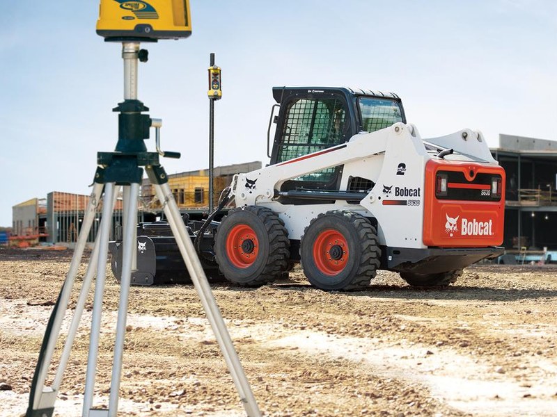 Skid steer with a machine receiver on its mast and a Spectra laser on an elevator tripod