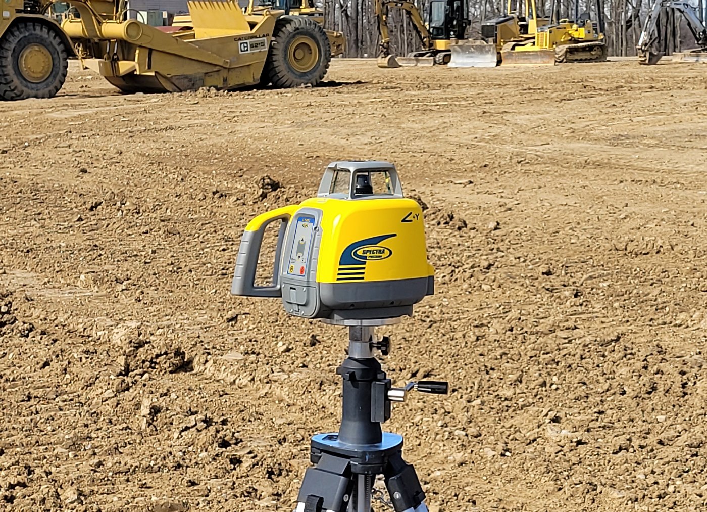 Spectra Precision LL1505C rotary laser on a tripod on a dirt site with a motor grader and dozer working behind it