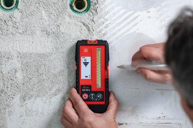 Leica RGR 300-D line laser receiver held against a wall while the user marks the laser line position with a pencil