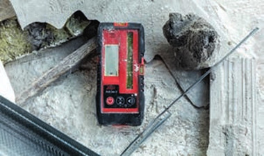 Leica RGR 300-D line laser receiver resting on a concrete slab beside a line laser beam